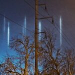 Vertikāli gaismas stabi naksnīgajās debesīs virs Bolderājas, Rīgā.