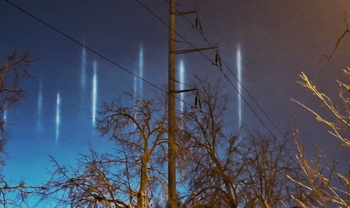 Vertikāli gaismas stabi naksnīgajās debesīs virs Bolderājas, Rīgā.